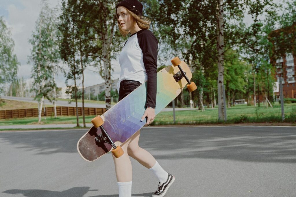 Teen girl carrying a longboard skateboard in an urban park, enjoying outdoor leisure activities.
